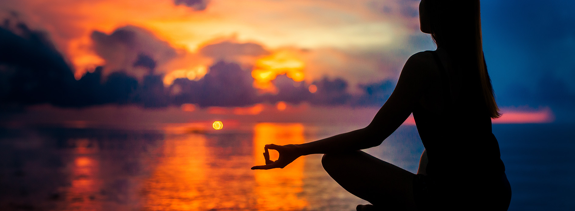 The image shows a person meditating at sunset with a scenic backdrop featuring vibrant colors and clouds.