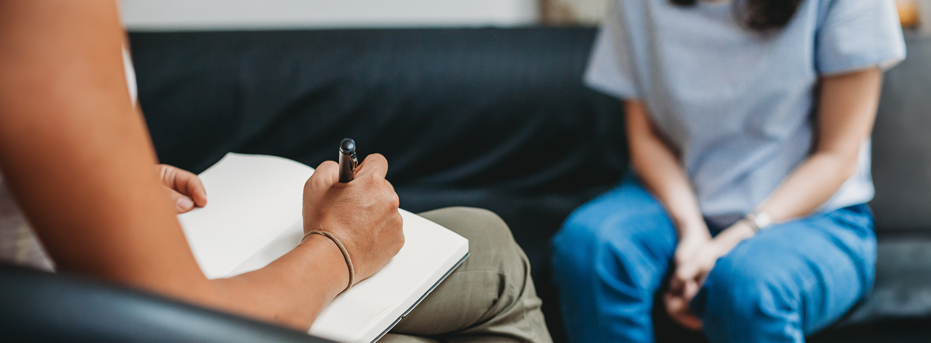 The image shows a group of people, possibly professionals given their attire and the setting that appears to be an office or professional environment. They are gathered around a table with a laptop on it, engaged in what seems to be a discussion or meeting.