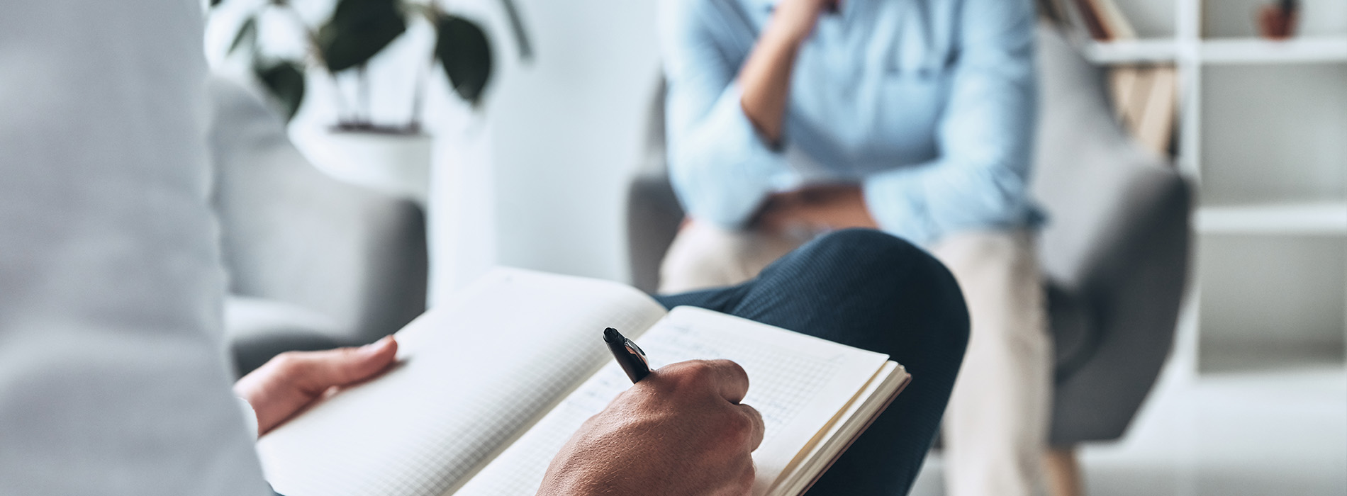 The image features a person sitting at a table with a notebook open in front of them, holding a pen, and appears to be engaged in writing or drawing.