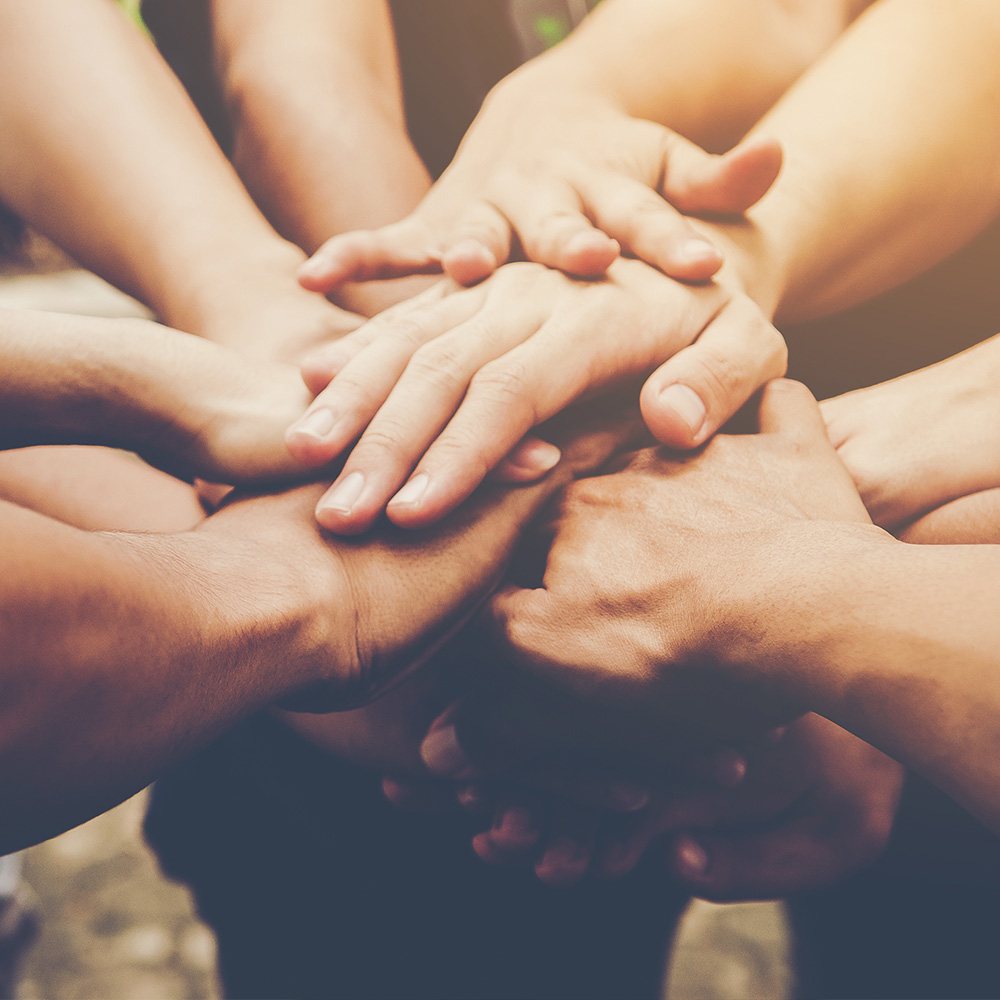 The image shows a group of people s hands joined together in a circle, symbolizing unity or support.