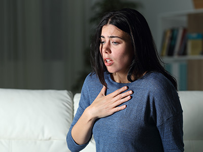A woman with her hand on her chest, appearing distressed, set against a blurred background.