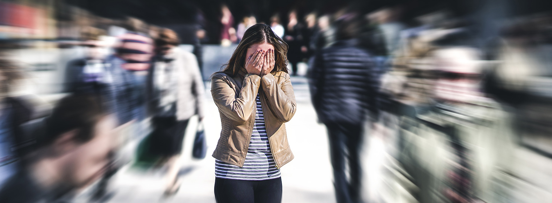 A woman in a striped shirt covering her face with her hands while standing on a street with a blurred background, possibly during a rainy day.