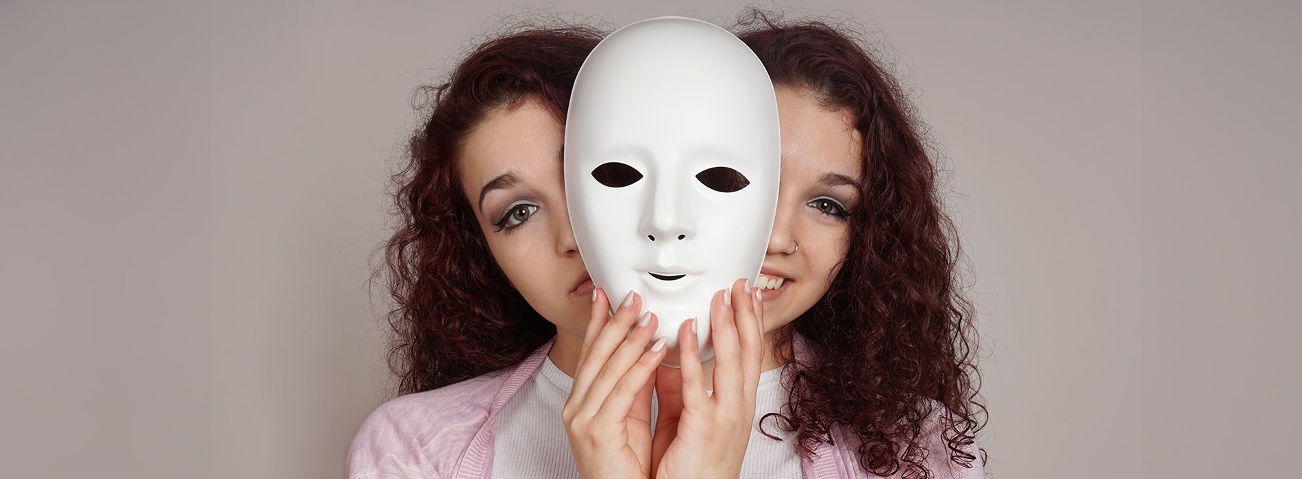 A person holding up a white mask with their face obscured behind it.