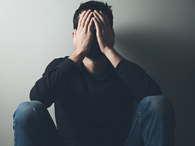 The image shows a person sitting on the floor with their hands covering their face, appearing distressed or upset.