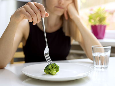 A person holding a fork over a plate of broccoli at a dining table.