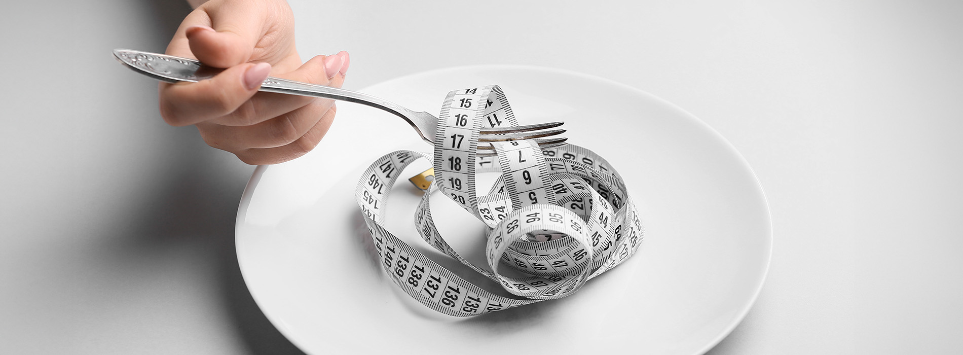 An alt tag for this image could be   A close-up photograph of a person s hand holding a measuring tape over a plate with food, set against a blurred background.