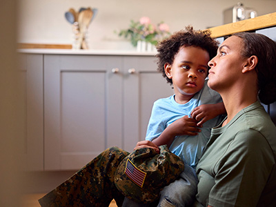 An adult woman in military uniform holding a young child while sitting indoors.