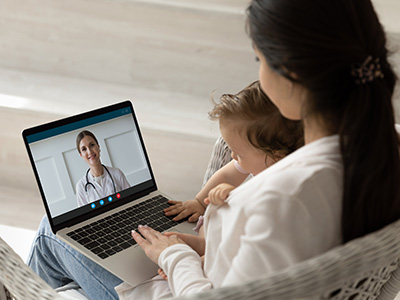 A woman using a laptop with a video call open, showing a child s face on the screen.