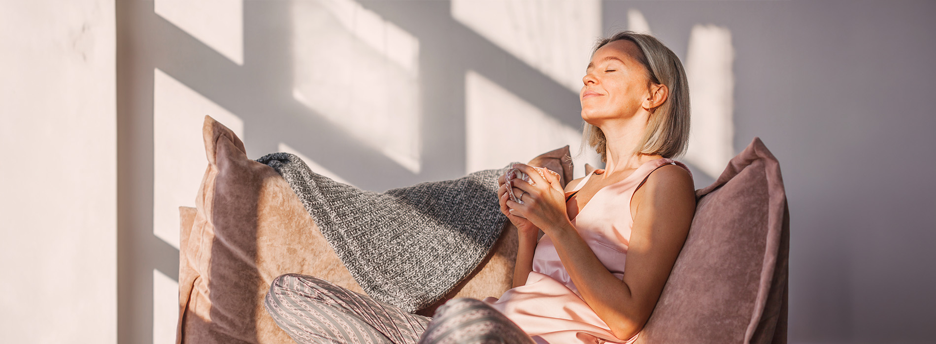 Woman sitting on a couch with hands clasped together, looking upwards, in a well-lit room.